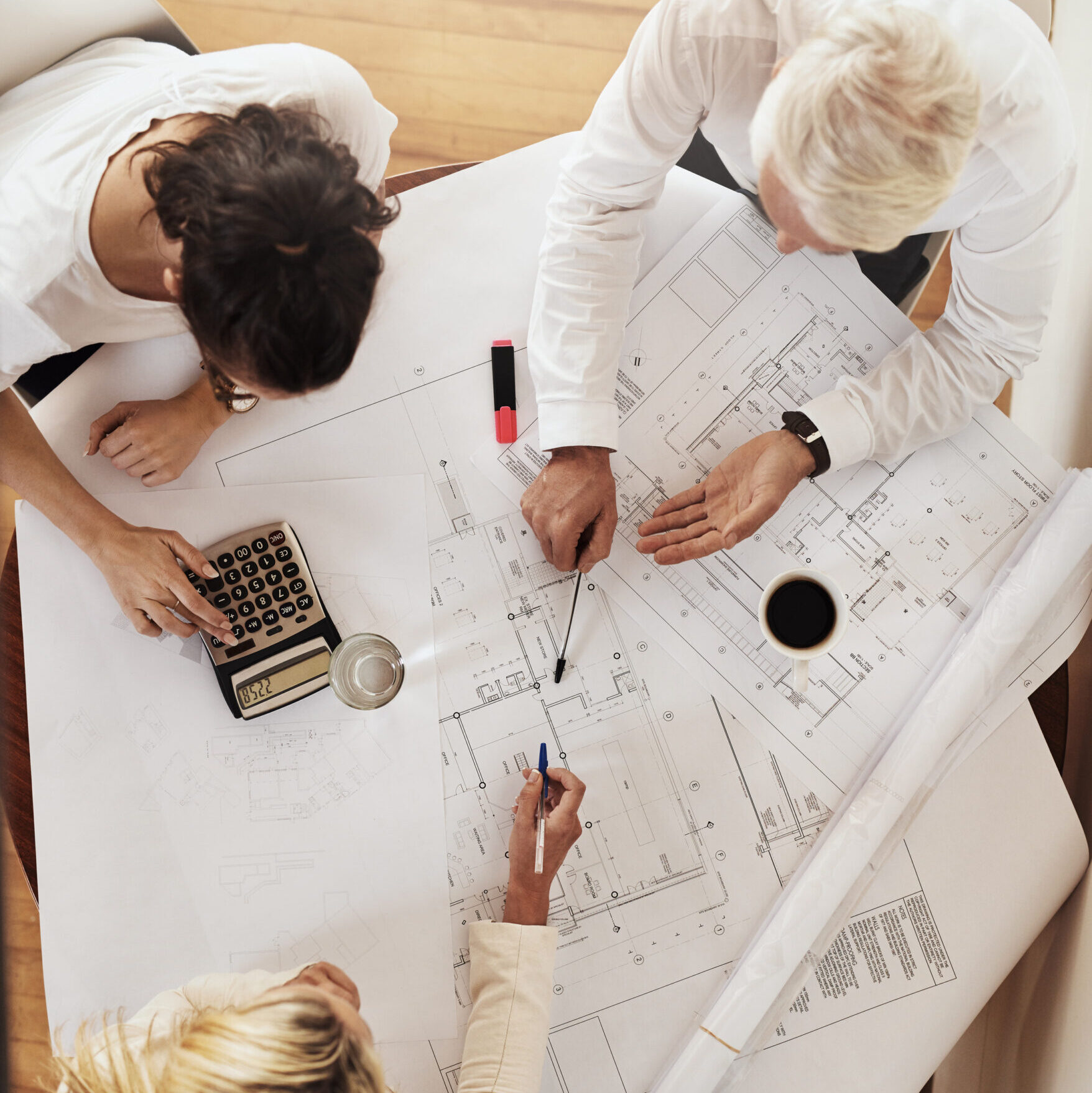 High angle shot of a group of architects working together on blueprints of a house around a table inside of a building.